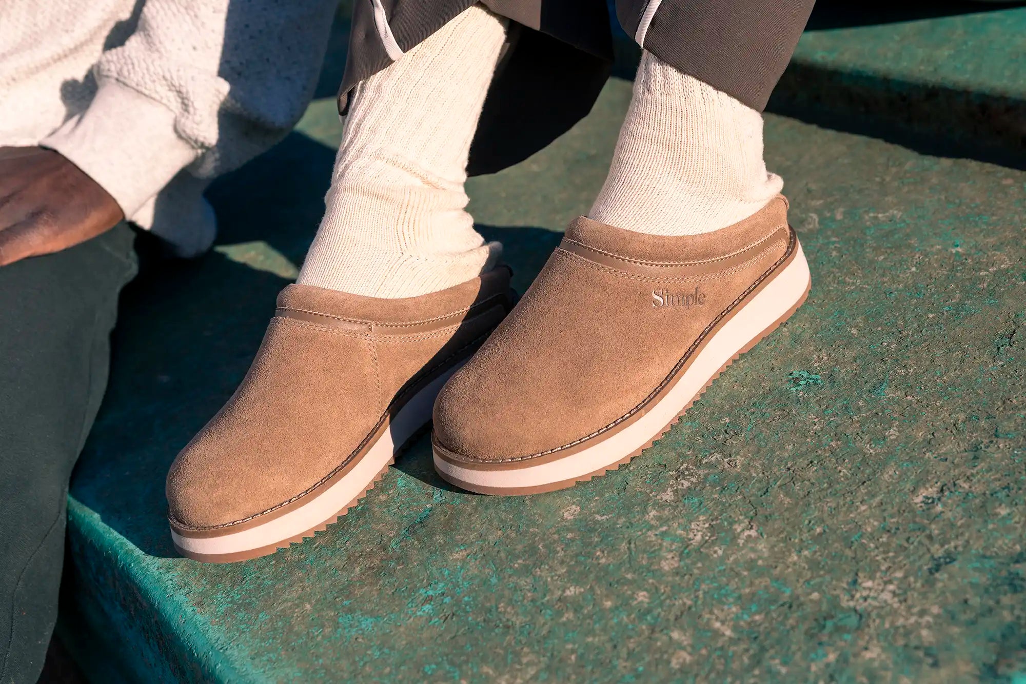 Brown slip-on shoes worn with white socks on a green surface