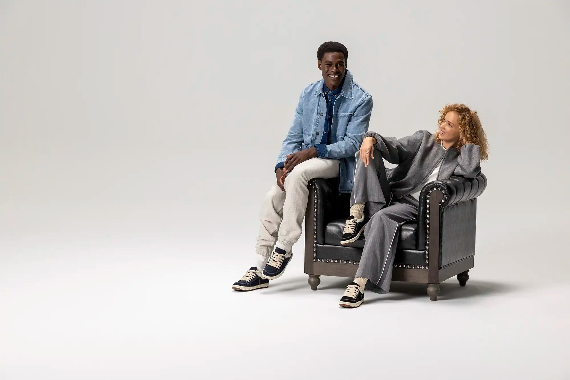 Two people sitting on a black leather armchair against a white background
