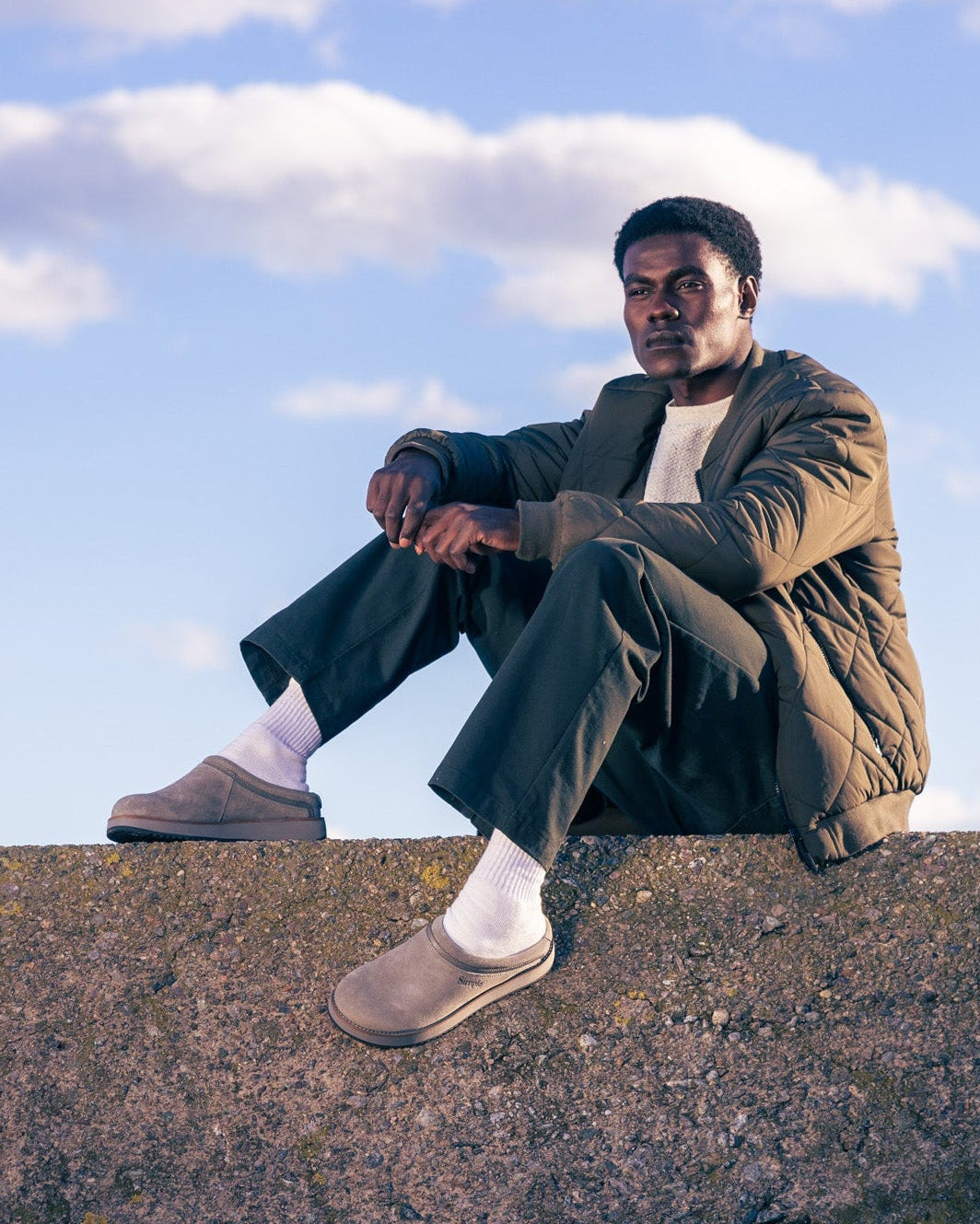 Person sitting on a concrete wall with a blue sky and clouds in the background.