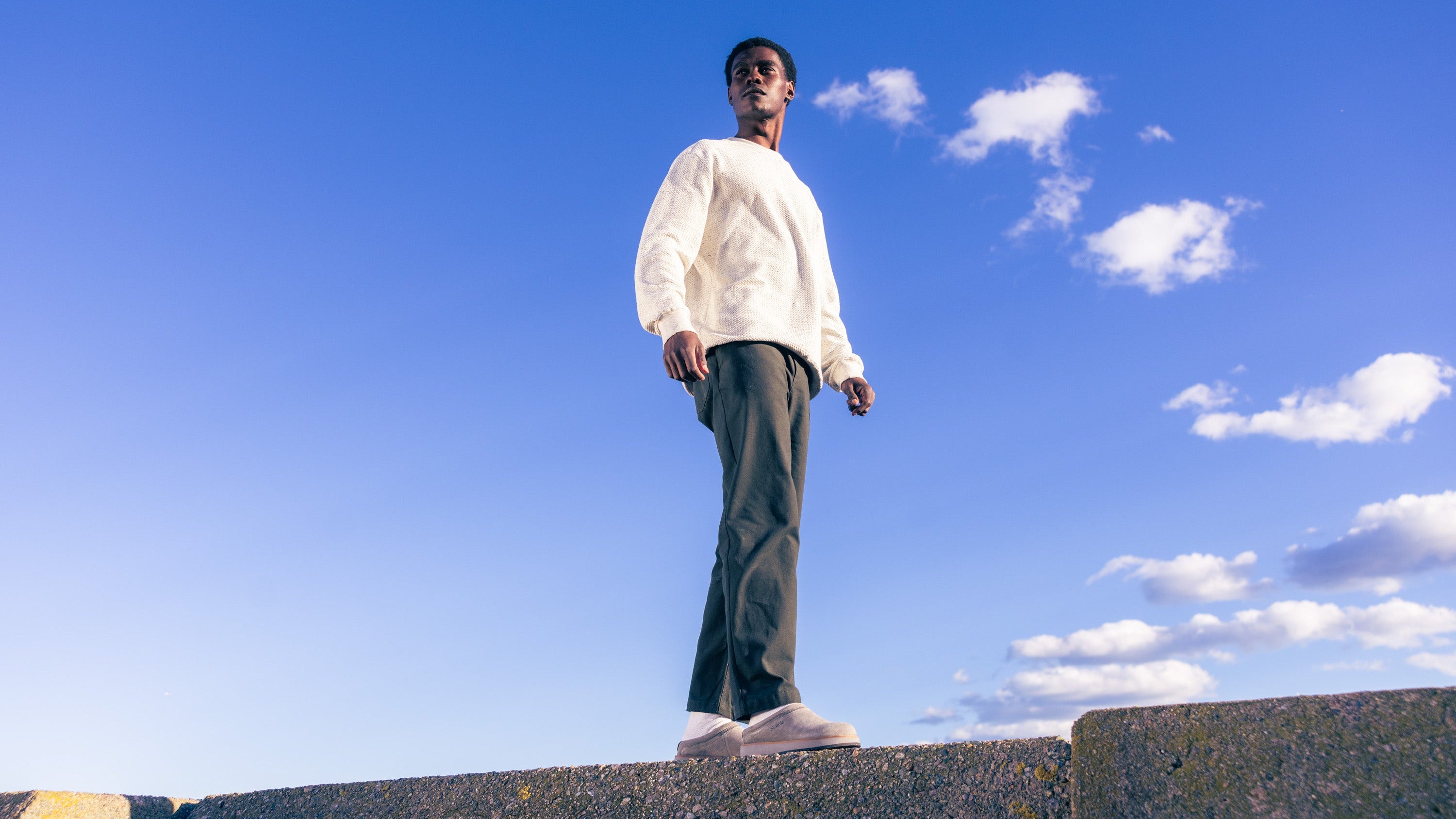 Person standing on a ledge with a clear blue sky and a few clouds in the background