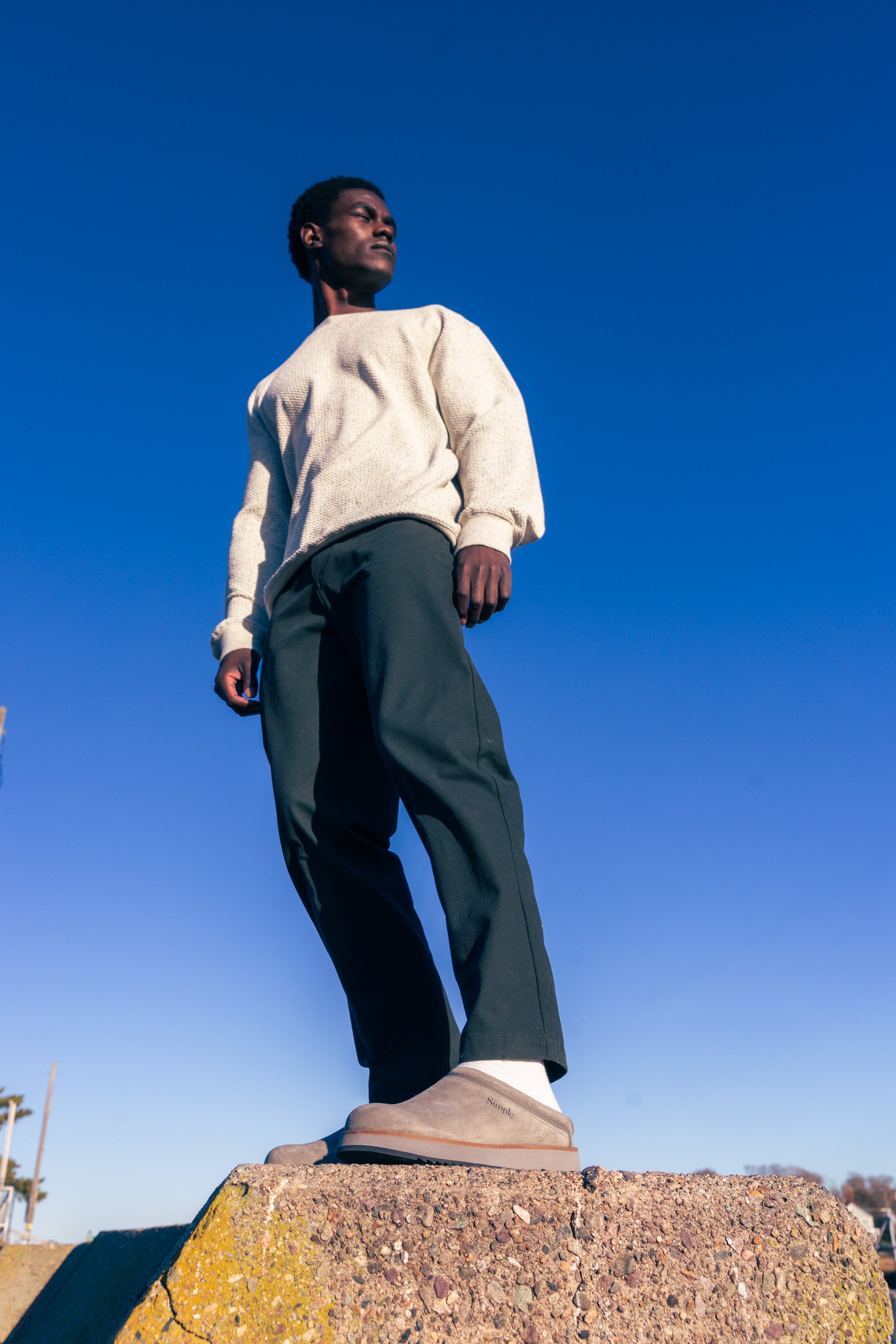 Person standing on a stone wall with a clear blue sky background