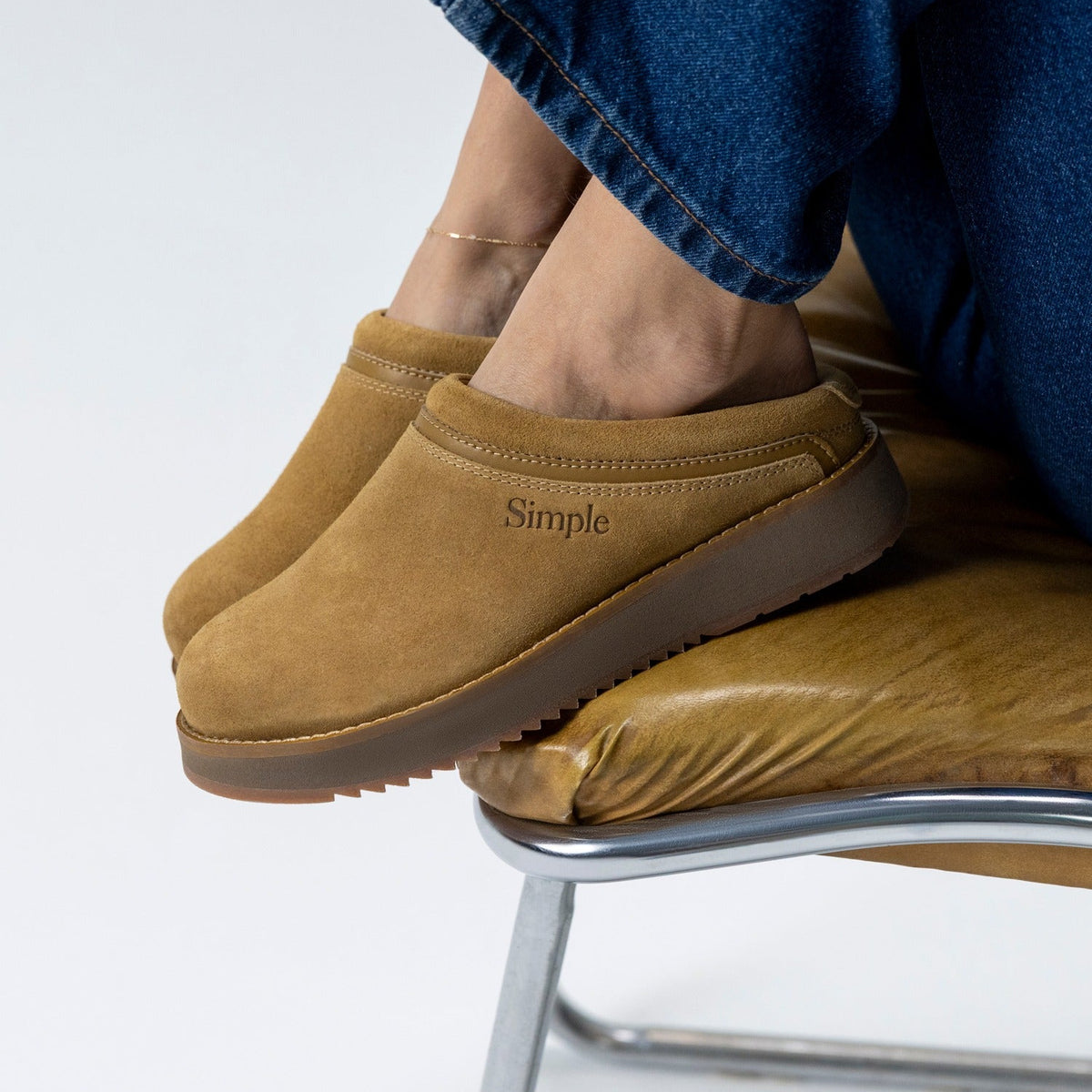 Brown slip-on shoes with 'Simple' branding worn by a person sitting on a chair.