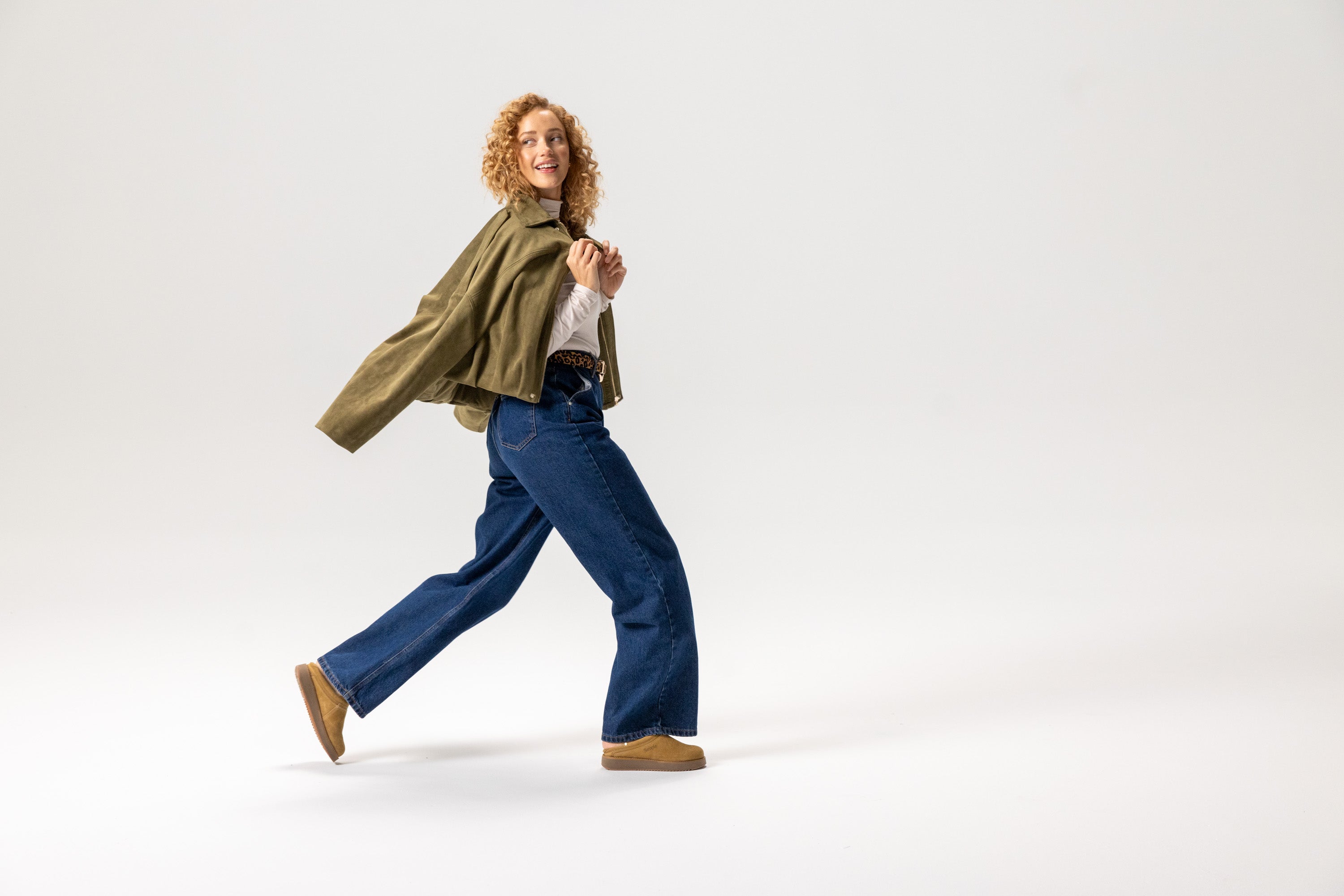 Woman in a green jacket and blue jeans walking on a white background