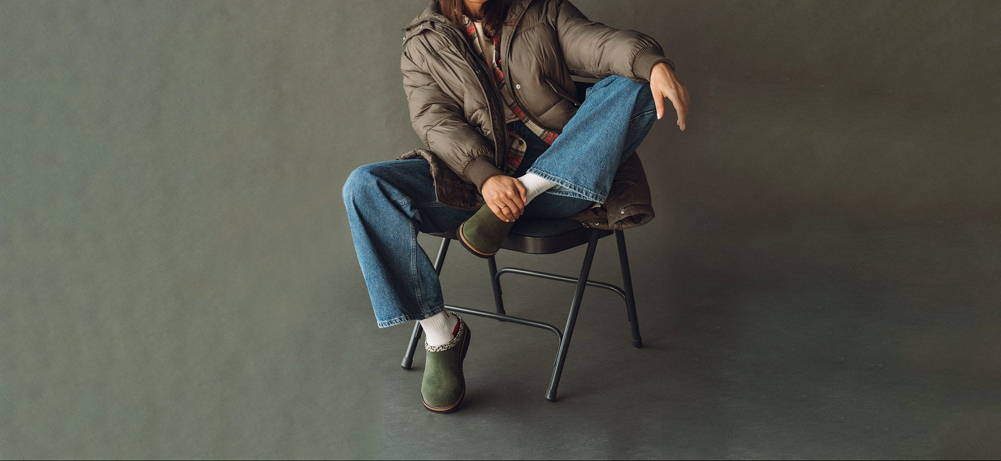 Person sitting on a chair wearing jeans and a jacket against a plain background
