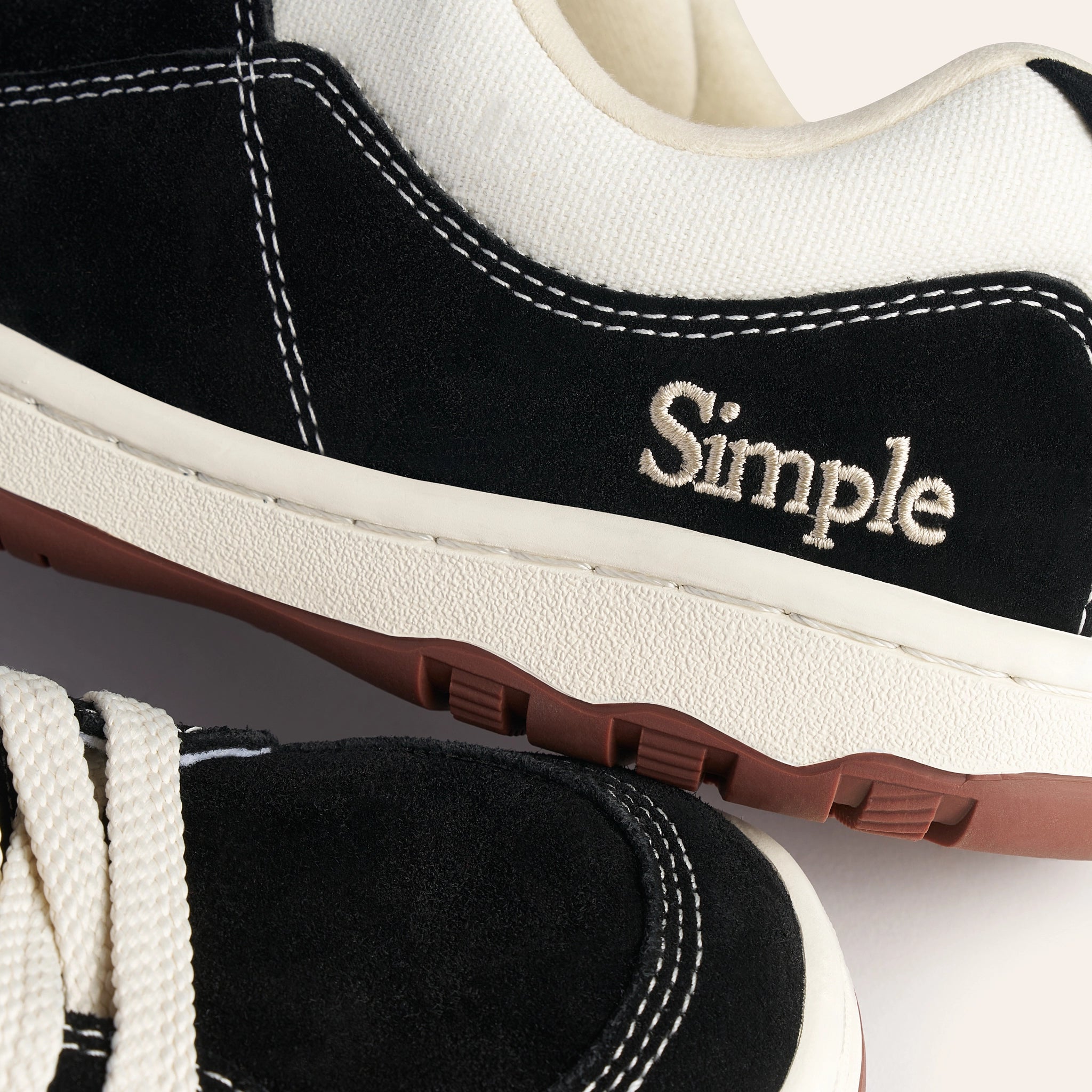 Black suede sneakers with off-white canvas, featuring Simple logo, durable rubber sole.