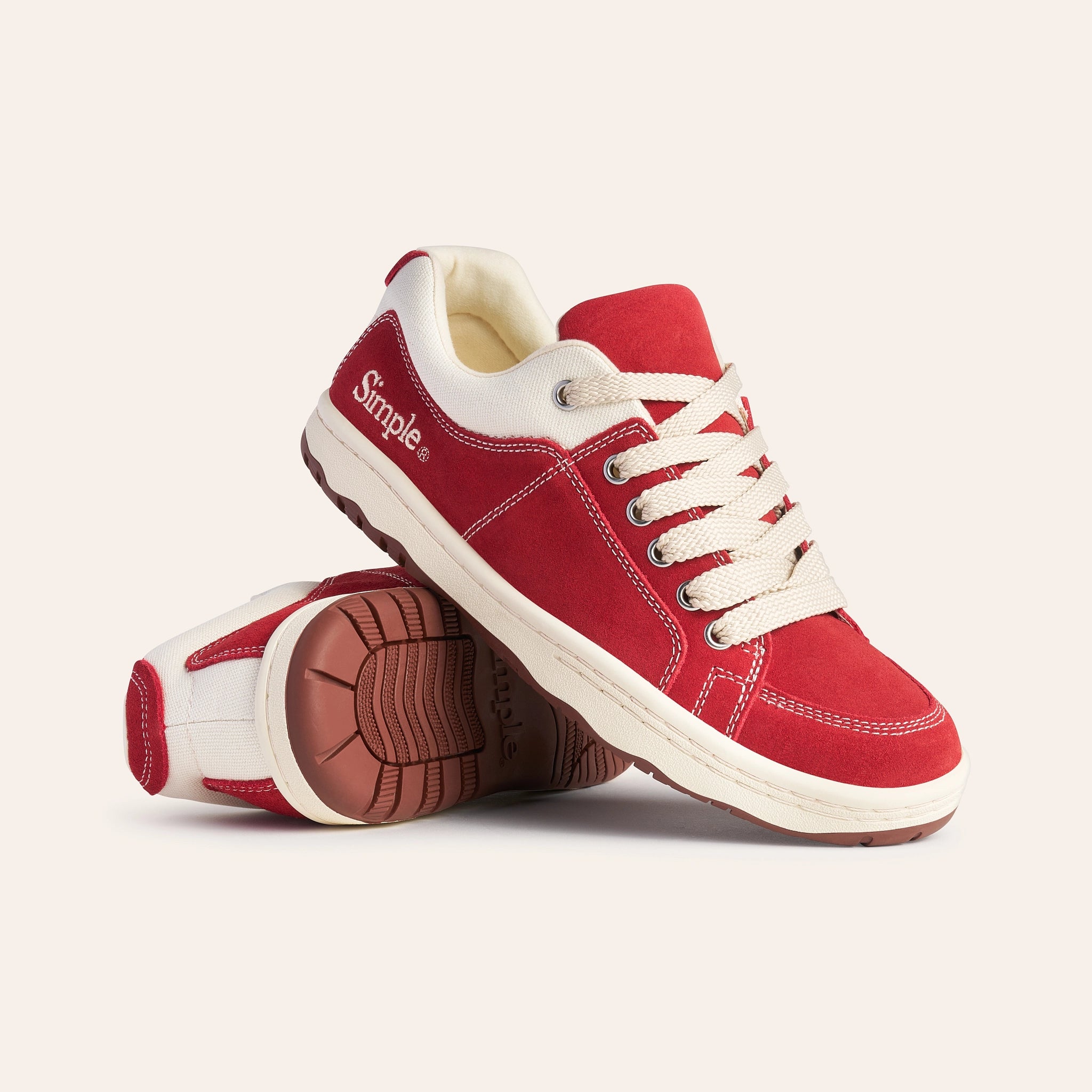 Red suede sneakers with white laces and cream accents, featuring a durable rubber sole and casual design.