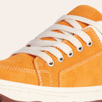Close-up of stylish orange suede sneakers with white laces and rubber sole.