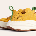 A close-up of a pair of yellow suede sneakers with green pull tabs, brown outsoles, and the brand name 'Simple' printed on the side, set against a light beige background.