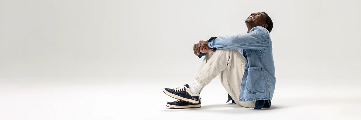 Person sitting on a white surface wearing a denim jacket and light-colored pants.