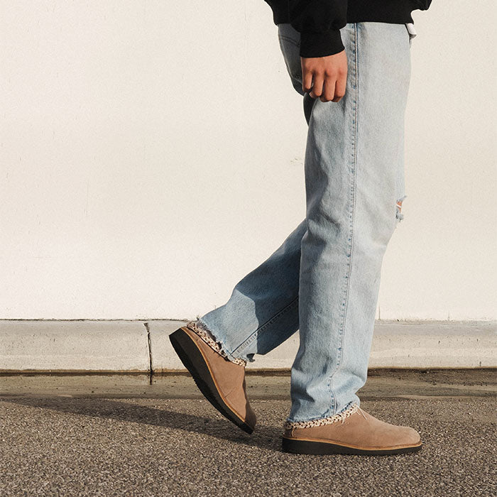 Person wearing light blue jeans and brown shoes on a plain background