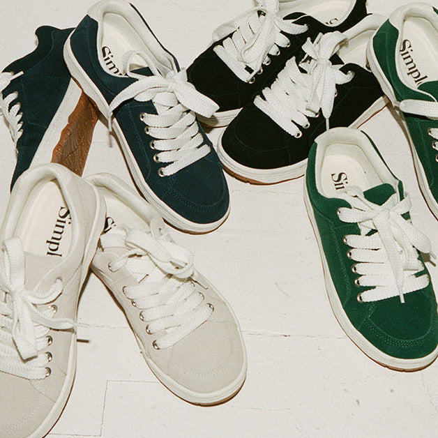 Green and white sneakers with 'Simple' branding on a light wooden floor.